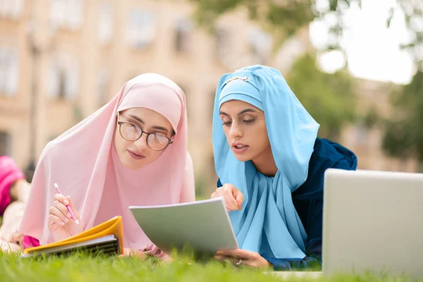 Two muslim students in hijab chilling on lane and reading