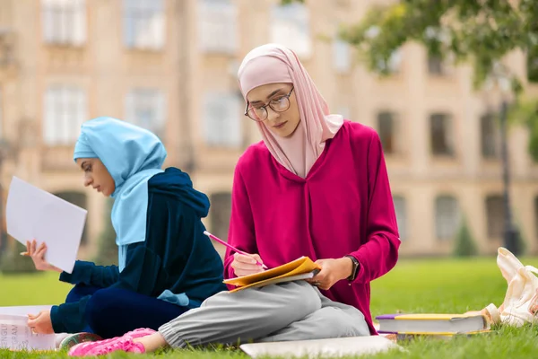 友人の近くで一生懸命勉強するメガネをかけたイスラム教徒の学生 — ストック写真