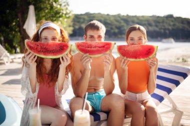 Nehir kenarında dinlenirken karpuz dilimlerini tutan milenyumlar