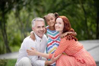 Loving foster parents hugging their lovely dark-skinned girl clipart
