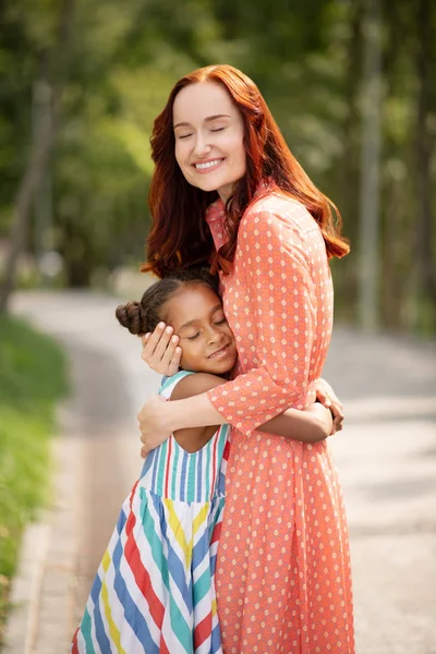 Beautiful red-haired woman smiling while hugging daughter — Stock Photo, Image