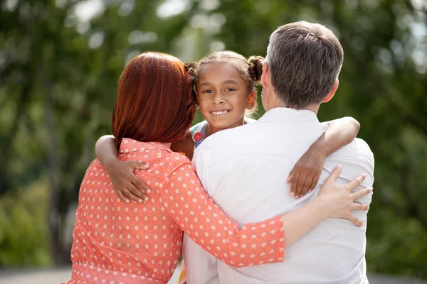 Chica de piel oscura sintiéndose feliz mientras abraza a sus padres adoptivos — Foto de Stock
