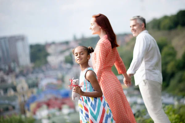 Adoptiv flicka klädd i ljusa klänning Walking med föräldrar — Stockfoto