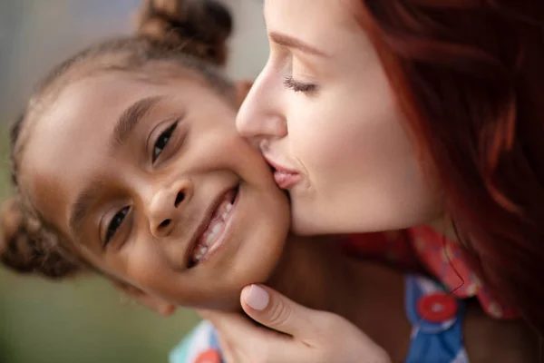 Adottato ragazza sorridente ampiamente mentre la madre la bacia — Foto Stock