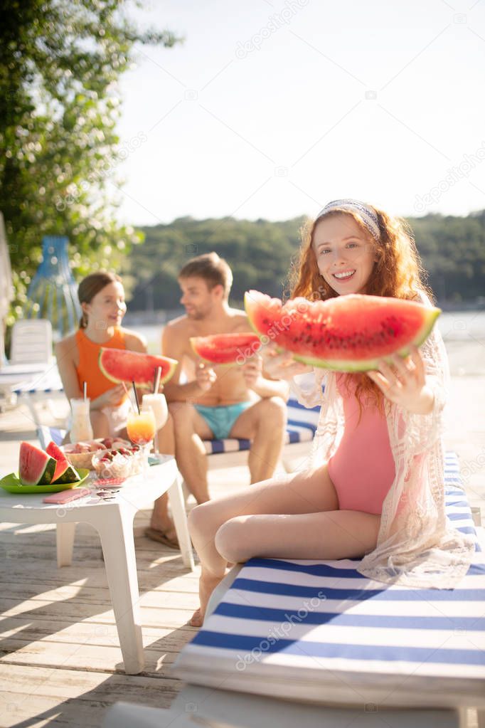 Slim red-haired woman holding big slice of watermelon