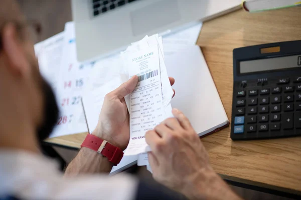 Bearded businessman sitting at the table and working on expenses