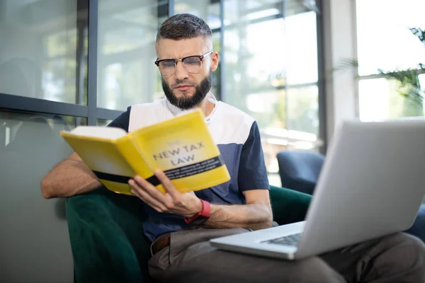 Homem de negócios barbudo usando óculos lendo livro de impostos — Fotografia de Stock