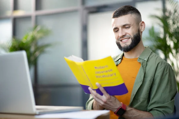 Бородатий молодий чоловік читає і вивчає іноземну мову — стокове фото