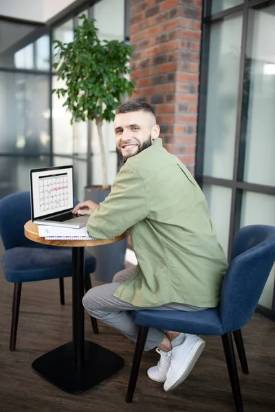 Hombre barbudo sentado en sillón y trabajando en el ordenador portátil — Foto de Stock