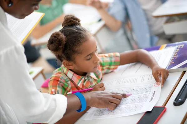 Dark-skinned schoolmeisje kijkt naar haar antwoordblad tijdens het schrijven van de test — Stockfoto