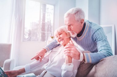 Bakım sakallı kocası dizüstü bilgisayar kullanarak onun sevimli yaşlı bayan sarılma