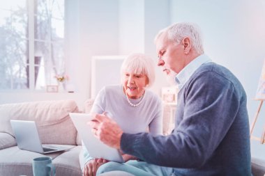 Gri saçlı emekli tablette fotoğraf gösteren koyu mavi kazak giyiyor