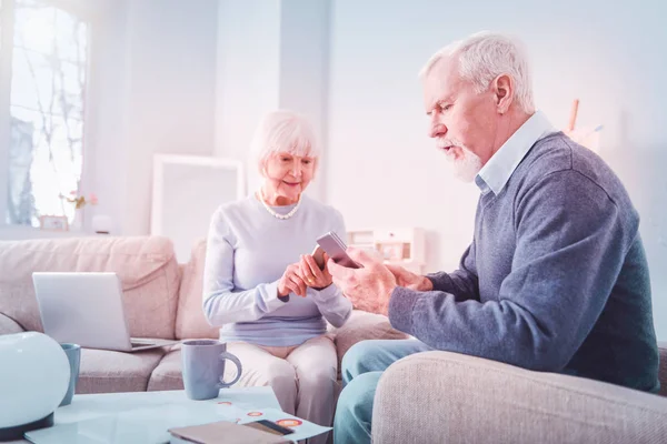 Modern pensioners using their smartphones sitting on sofa at home — Stock Photo, Image