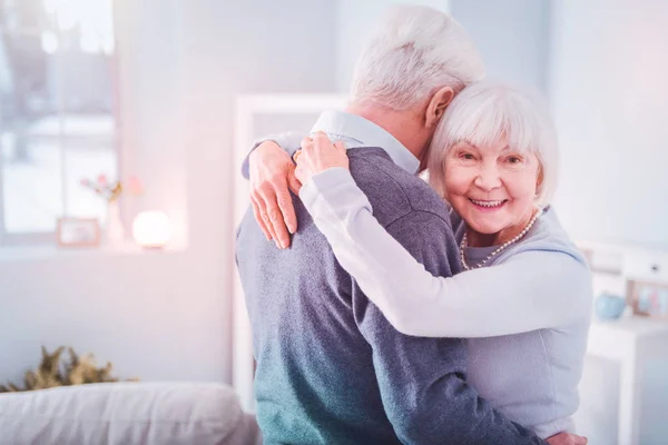 Beaming retired woman feeling happy hugging her grey-haired husband — Stock Photo, Image