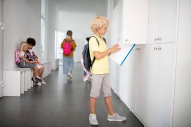 Dolaptan not defteri alan sırt çantası giyen sarışın çocuk