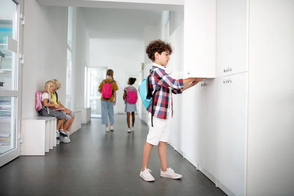 Colegial con mochila poniendo cosas dentro del casillero — Foto de Stock