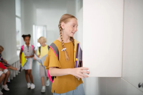 Chica sonriente con mochila abriendo su casillero en la escuela — Foto de Stock