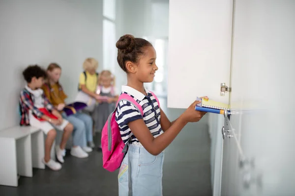 Leende mörkhyade flicka sätta böcker inuti Locker — Stockfoto