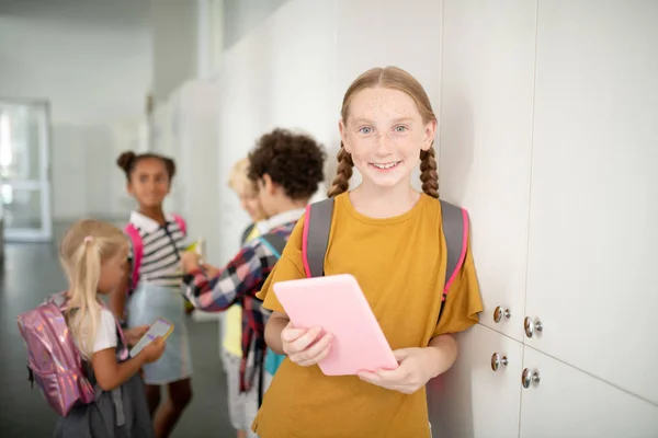 Mädchen mit Rucksack hält rosa Tablet in der Nähe von Schließfächern — Stockfoto