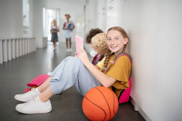 Gadis dengan tablet duduk dekat bola basket di lorong sekolah — Stok Foto