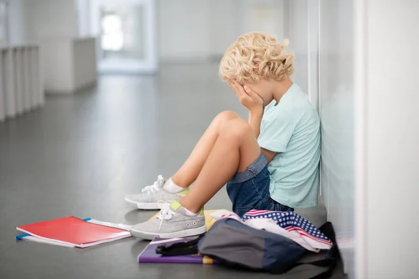 Blonde curly boy sitting on the floor and crying after bullying — Stock Photo, Image