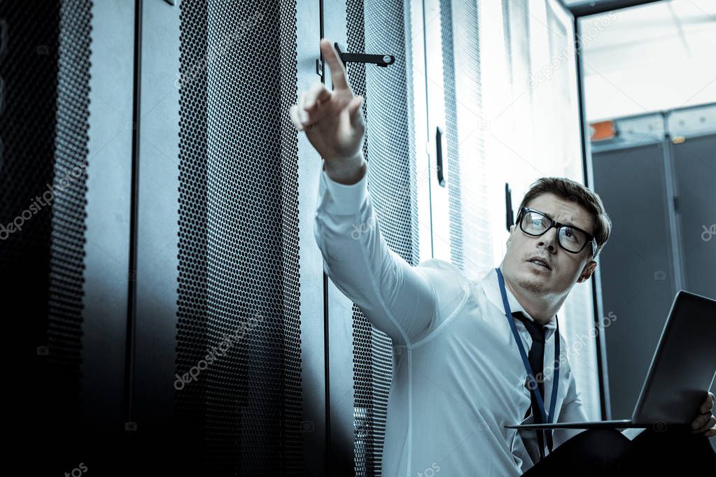 Short-haired man in eyewear pointing to the security panel
