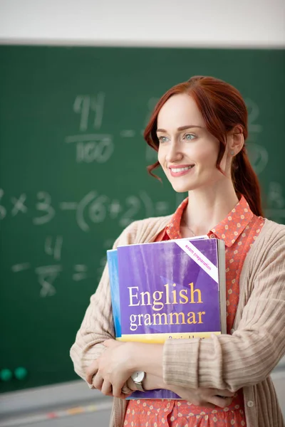 Beaming teacher holding books standing in classroom — Stock Photo, Image