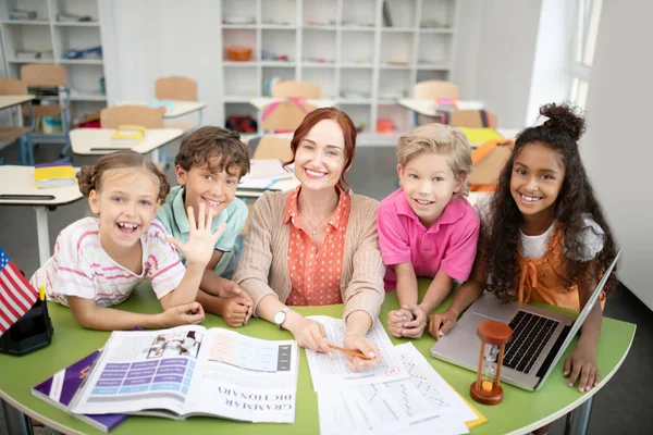 Children standing around their friendly smiling teacher — Stock Photo, Image