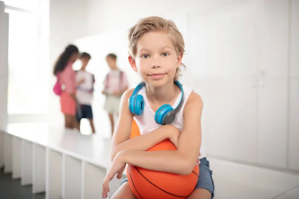 Niño guapo con auriculares en el cuello sosteniendo pelota de baloncesto — Foto de Stock