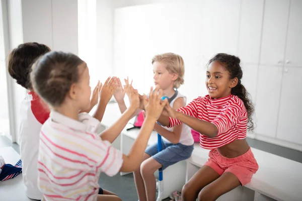 Niños y niñas aplaudiendo mientras están sentados en el vestuario — Foto de Stock