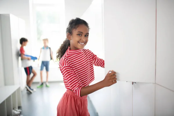 Χαμογελαστή μελαχρινή κορίτσι στέκεται κοντά στο ντουλάπι στο σχολείο — Φωτογραφία Αρχείου