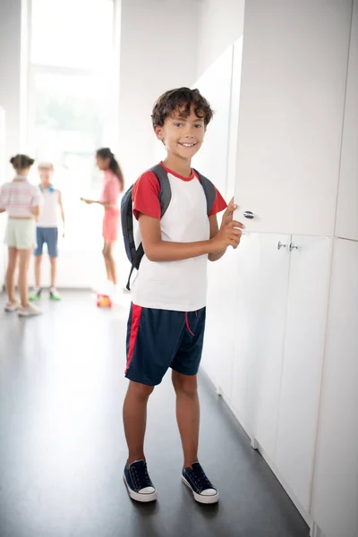 Niño de cabello oscuro usando ropa deportiva de pie cerca del casillero — Foto de Stock