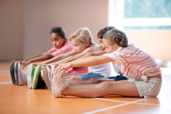 Boys and girl reaching for toes while stretching their bodies — Stock Photo, Image