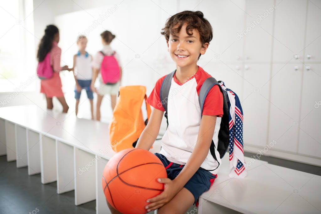 Dark-haired boy wearing backpack holding basketball ball