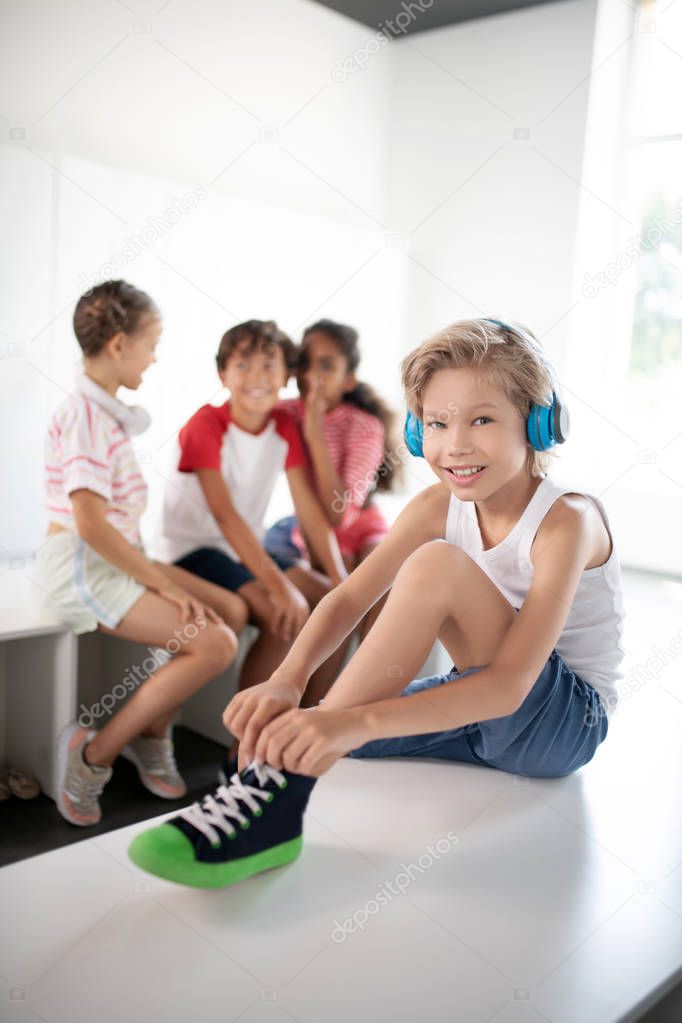 Cheerful boy listening to music while lacing sneakers
