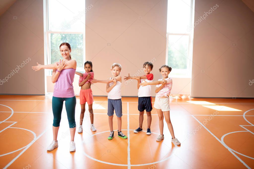 PE teacher and children stretching arms before starting physical training
