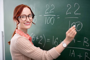 Deneyimli matematik öğretmeni tebeşir ile tahta yakınında duruyor