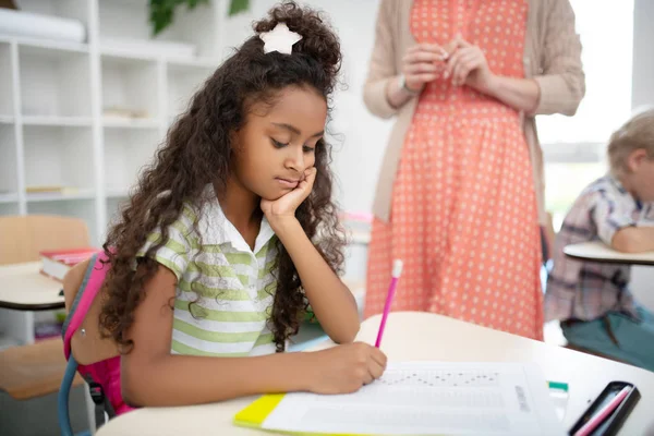 Cute dark-skinned girl holding pencil while writing test — Stock Photo, Image