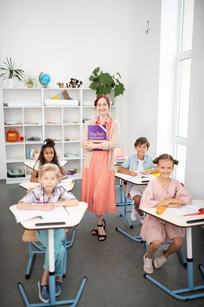 Professora de inglês sorridente em pé na sala de aula com os alunos — Fotografia de Stock