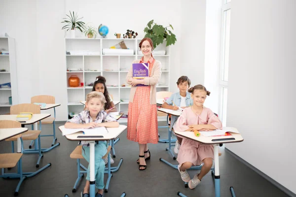 Cuatro alumnos diligentes sentados en los escritorios cerca del profesor —  Fotos de Stock