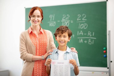 Kızıl saçlı öğretmen gülümseyerek ve akıllı öğrencisine sarılıyor
