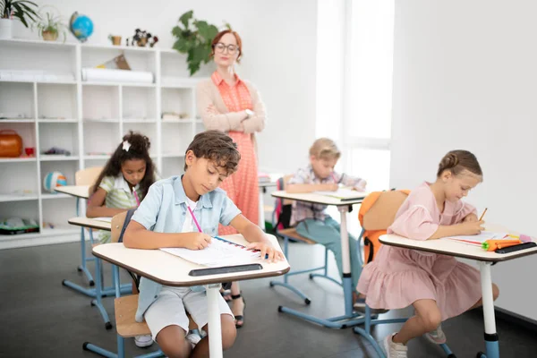 Учитель в очках смотрит, как дети пишут тесты — стоковое фото