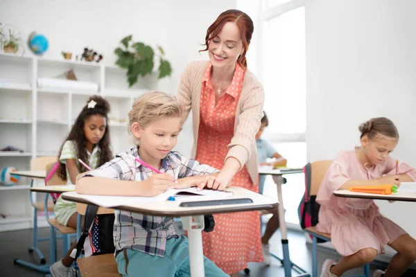 Pleasant teacher of primary school coming to her pupil Stock Image