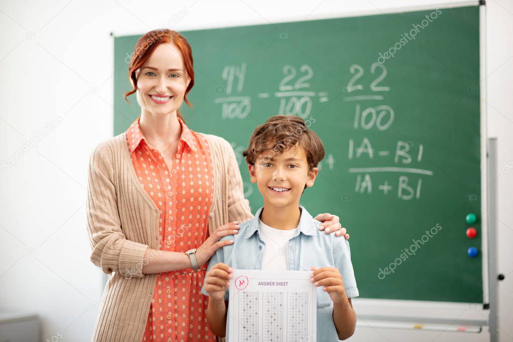 Red-haired teacher smiling and hugging her clever pupil