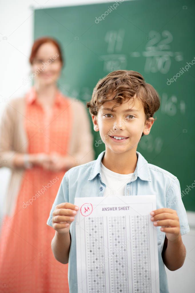 Dark-haired boy standing near blackboard with answer sheet