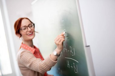 Tahtaya yazarken tebeşir tutan gözlük takan öğretmen