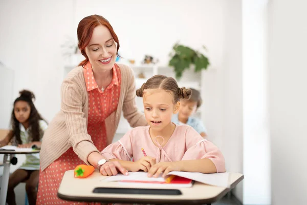 Profesora sonriente ayudando a una chica a escribir cartas — Foto de Stock