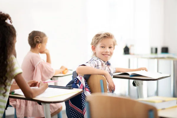 Snygg blond-haired pojke sitter vid skrivbordet i klassrummet — Stockfoto