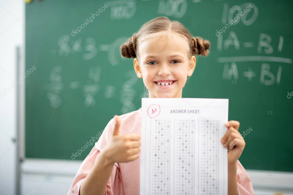 Smiling girl holding her answer sheet with excellent mark
