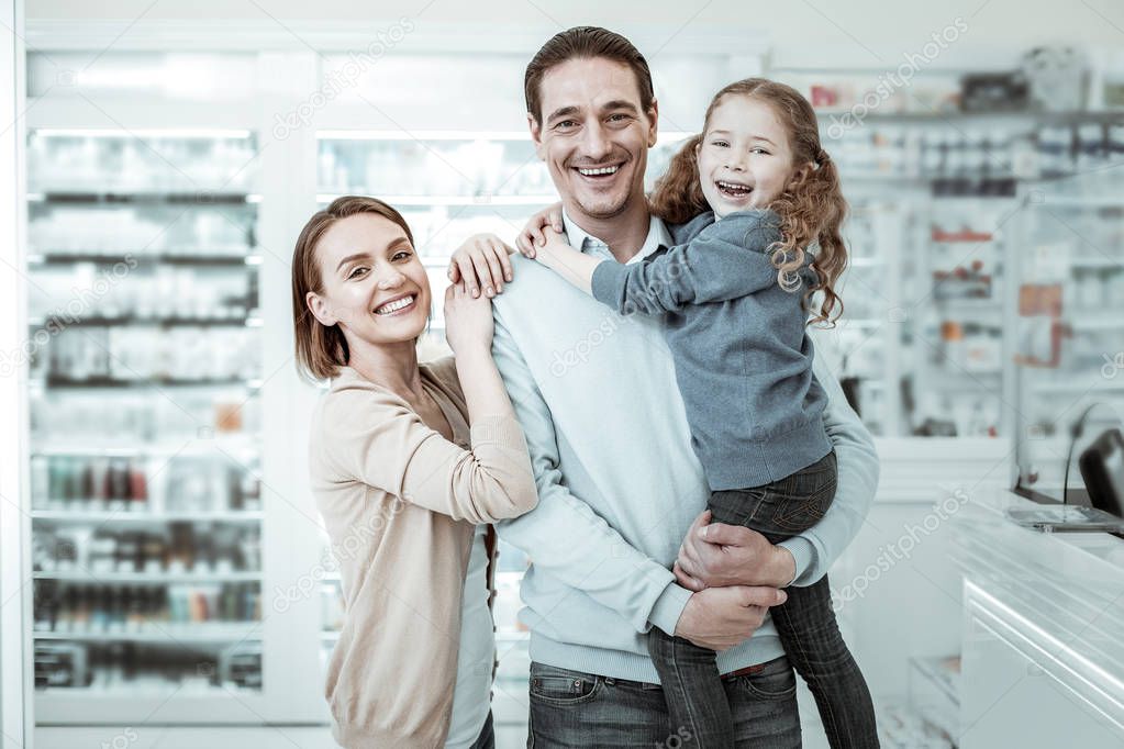 A beamingly smiling family sharing cuddles near the pharmacy checkout
